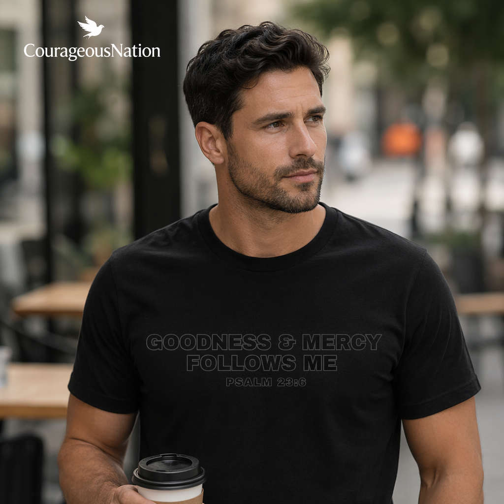 Man wearing a black t-shirt with Goodness and Mercy Follows Me Psalm 23: 6, holding a coffee cup outdoors.