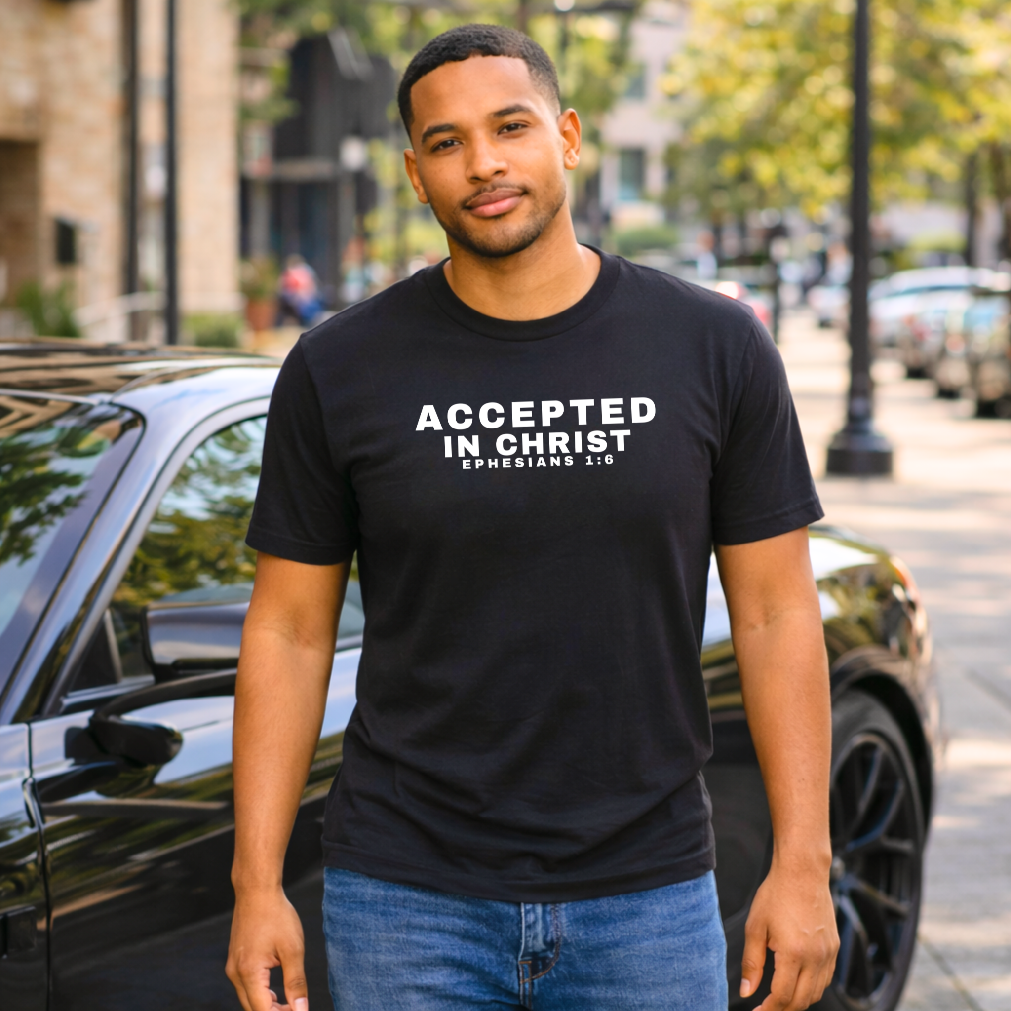 Man wearing a black t-shirt with 'Accepted in Christ' text, standing on a street.