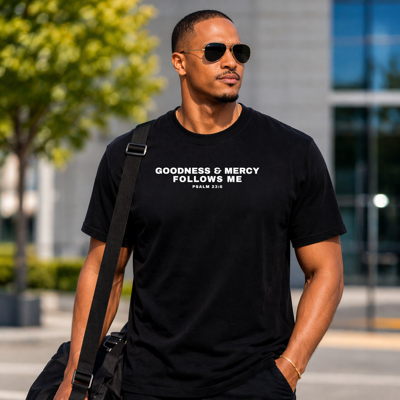 Man wearing a black t-shirt with Goodness and Mercy Follows Me Psalm 23:6, standing outdoors.