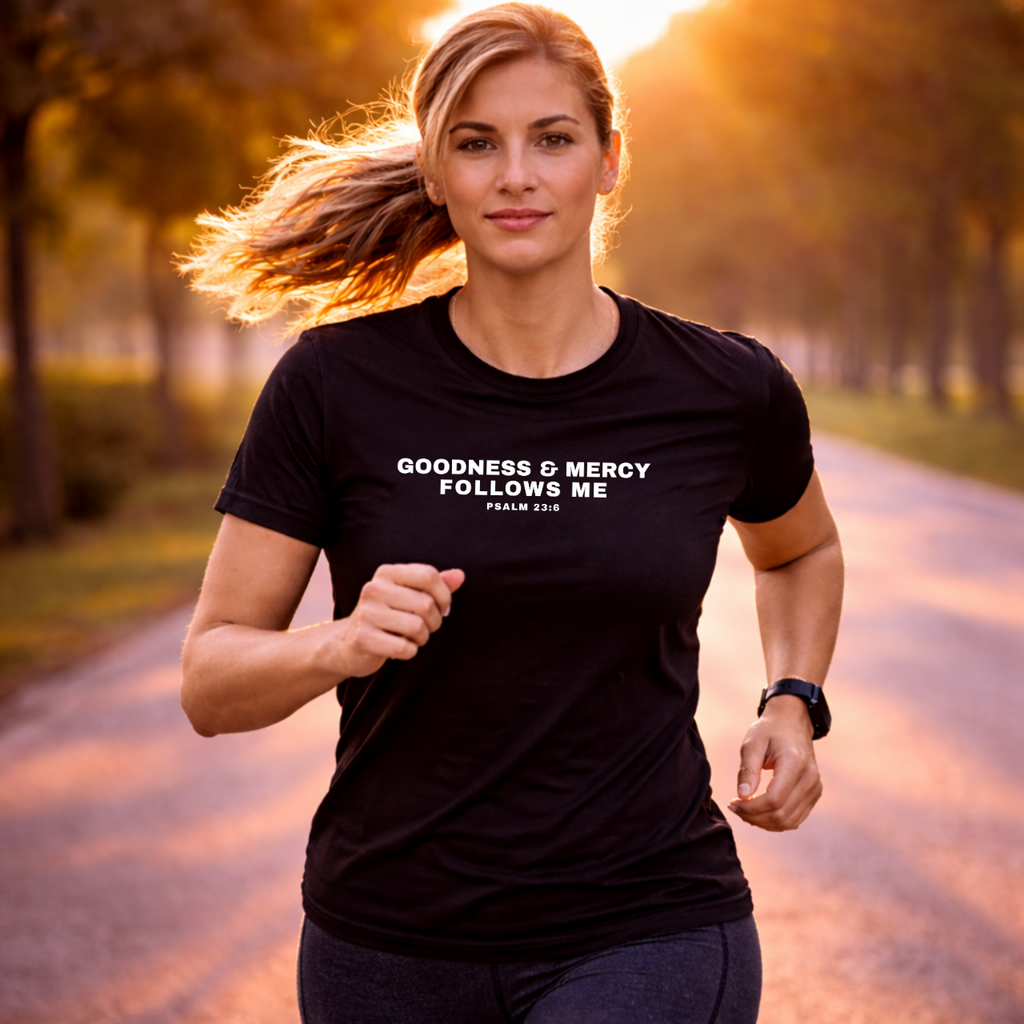 Woman running outdoors wearing a black t-shirt with Goodness and Mercy Follows Me Psalm 23:6